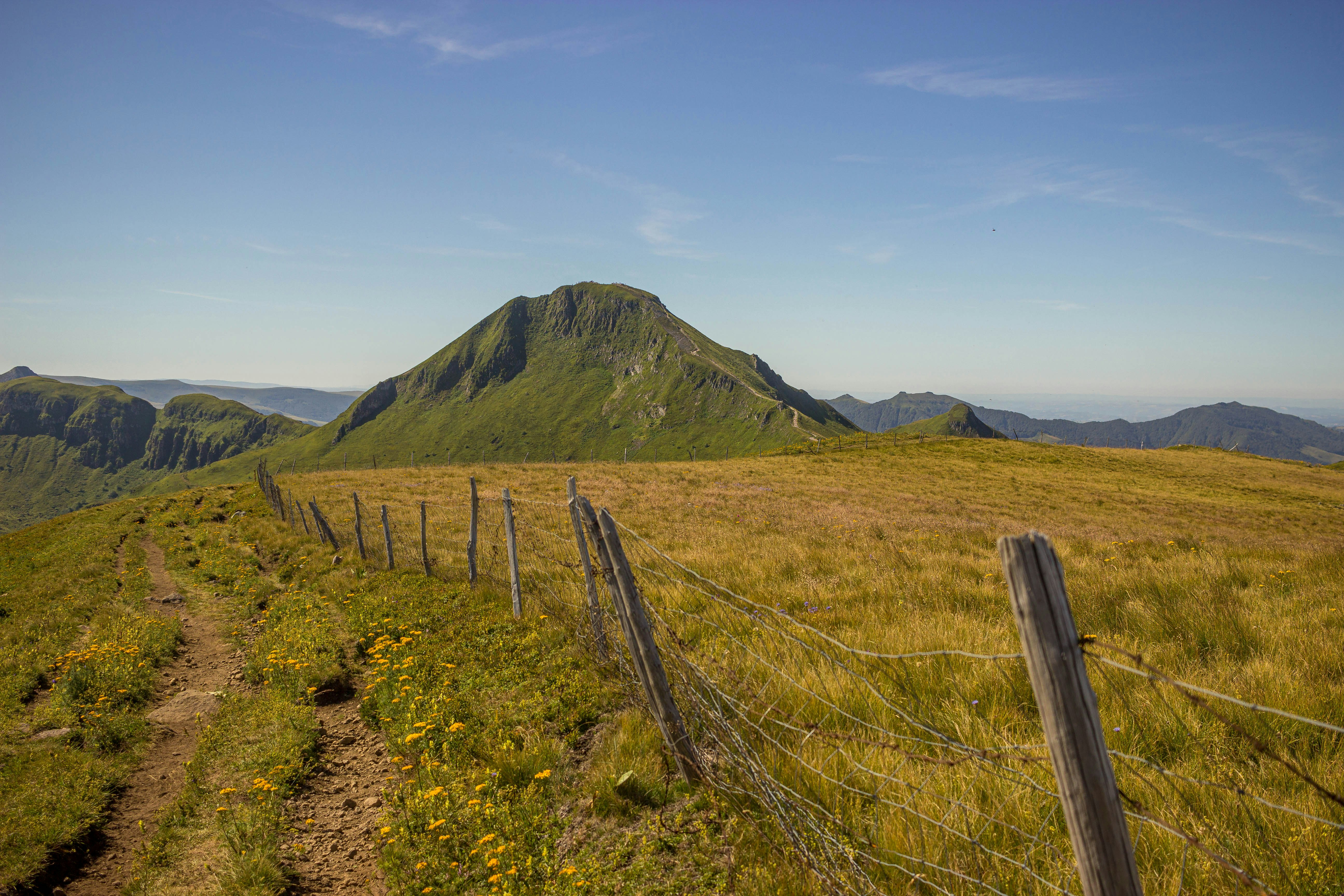 green grass field near mountain under blue sky during daytime